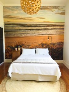 A beach mural makes a great accent wall and provides a headboard that takes up zero floor space.