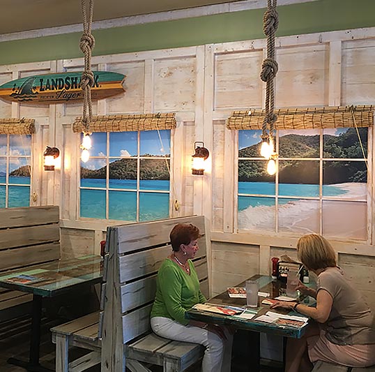 When your fast-casual restaurant chain is called Hurricane Grill and Wings you can bet that the interior is going to have a beach hut kind of vibe. That's exactly what was achieved by installing a tropical beach view wallpaper mural behind faux windows.